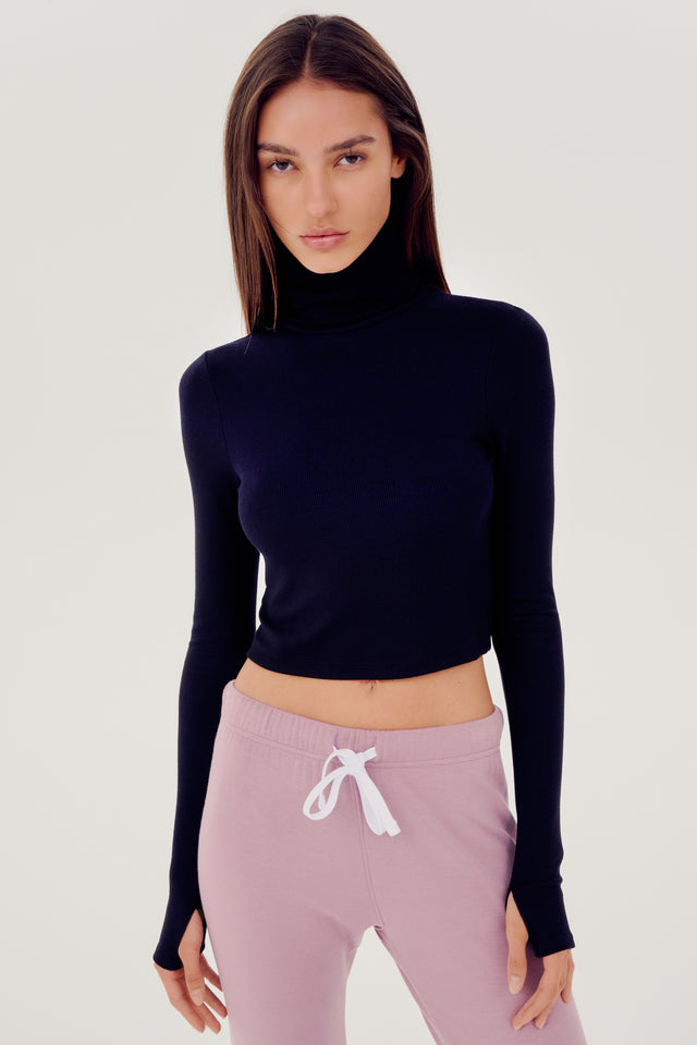 The model is wearing a black SPLITS59 Jackson Rib Cropped Turtleneck top and high waist leggings.