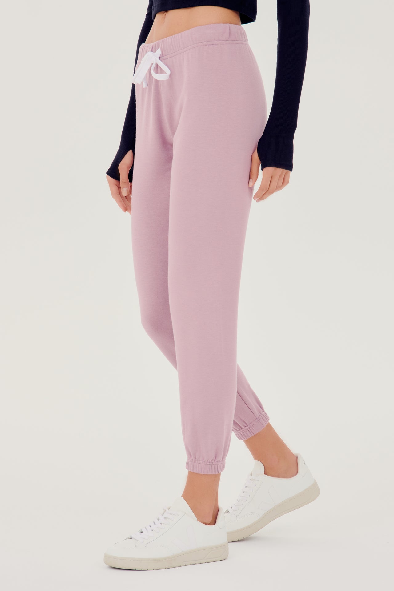 Front side view of woman wearing light pink sweatpant jogger with white drawstring and black turtleneck cropped long sleeve paired with white shoes