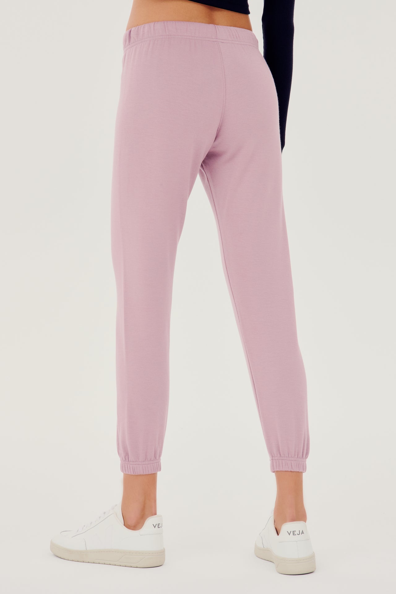 Back view of woman wearing light pink sweatpant jogger with white drawstring and black turtleneck cropped long sleeve paired with white shoes