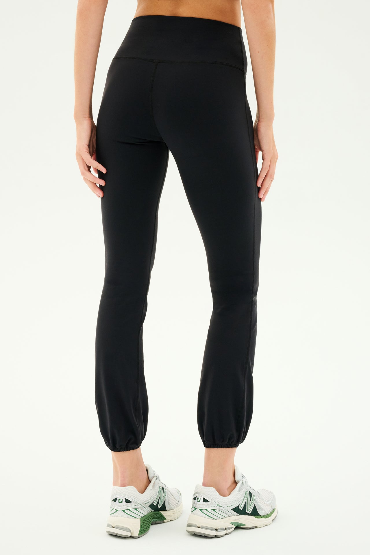 Person wearing the SPLITS59 Icon High Waist Supplex Legging in black paired with white athletic shoes, shown from the back. The plain white background emphasizes the slim fit of the legging.