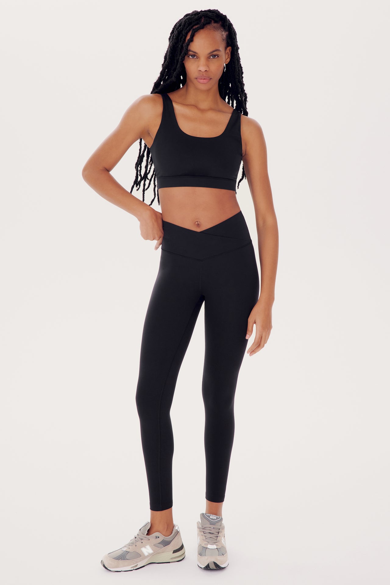 A woman in a SPLITS59 Sprint Rigor Bra in Black and athletic wear stands confidently against a white background, ready for multi-sport performance.