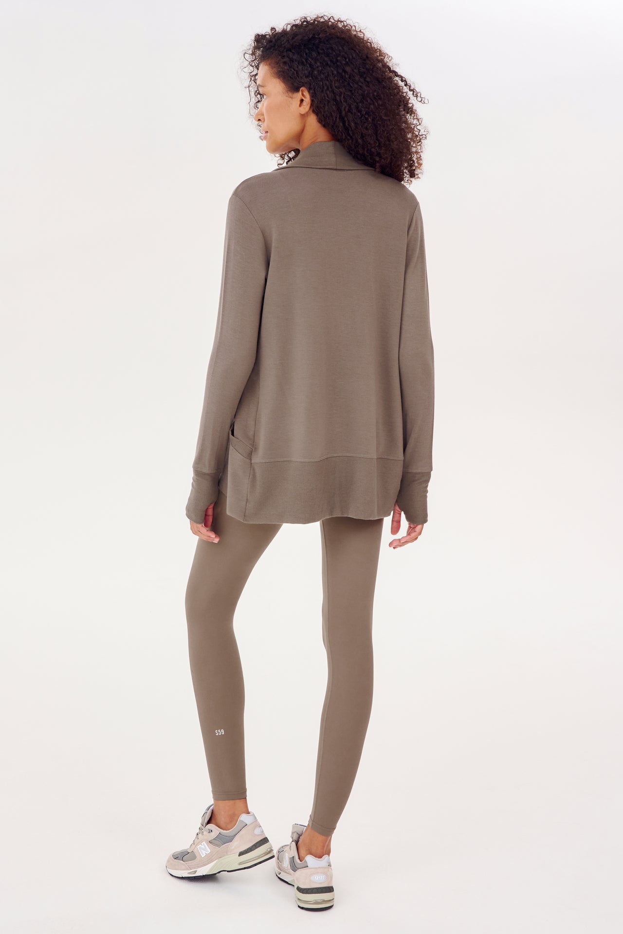 The back view of a woman wearing a SPLITS59 Celine Fleece Cardigan - Lentil with thumbhole sleeves and leggings, both made in Los Angeles.