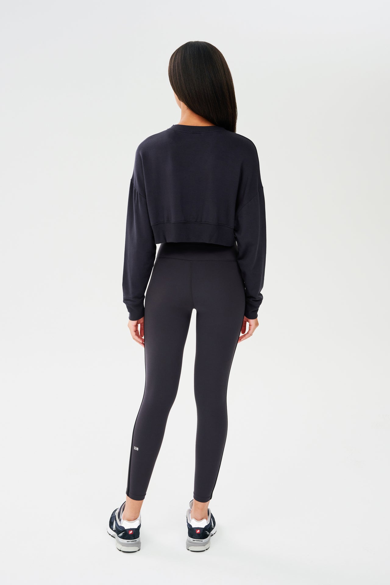 The back view of a woman wearing an athletic SPLITS59 Noah Fleece Crop Sweatshirt in Graphite and leggings.