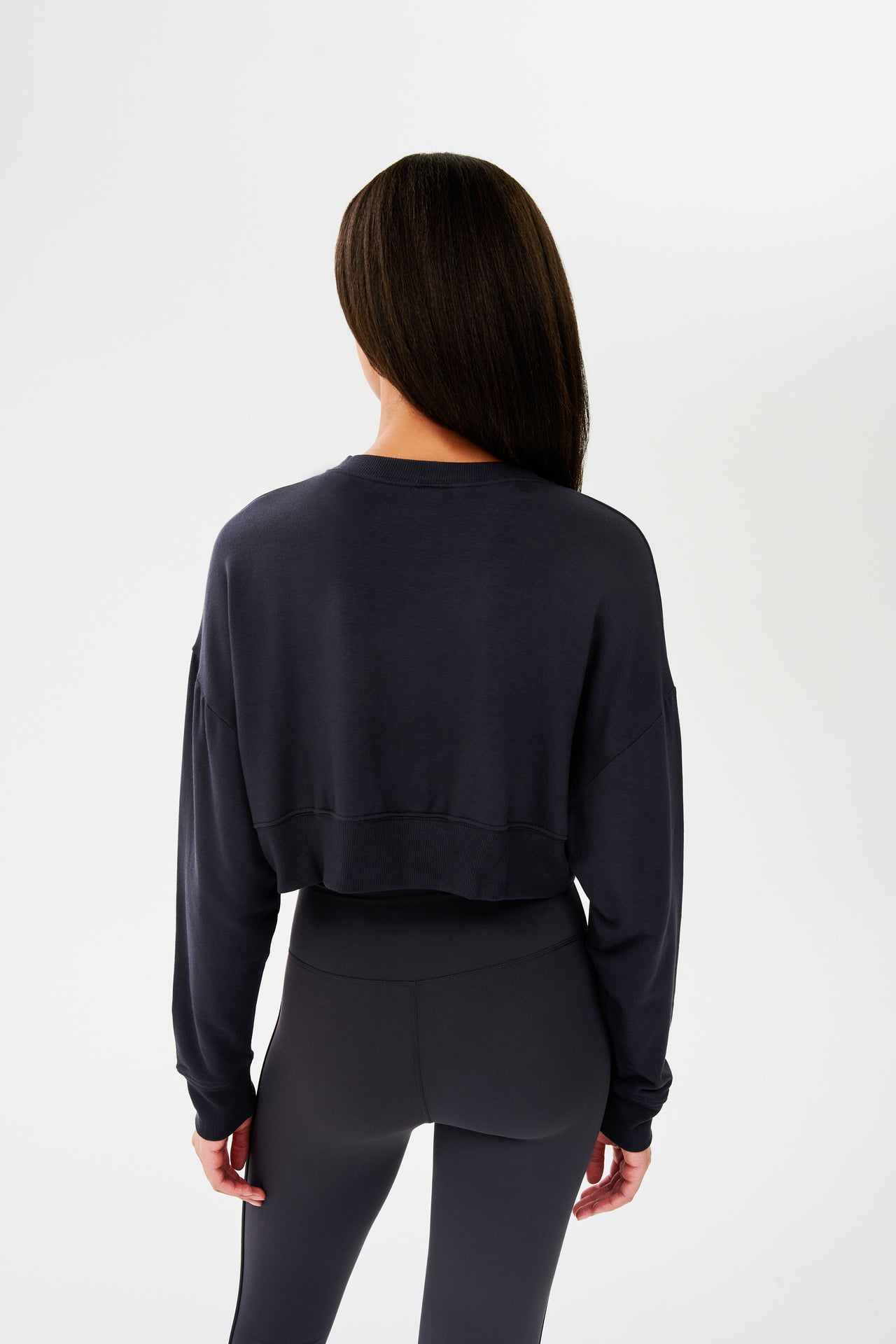 The back view of a woman wearing black leggings and a SPLITS59 Noah Fleece Crop Sweatshirt in Graphite.