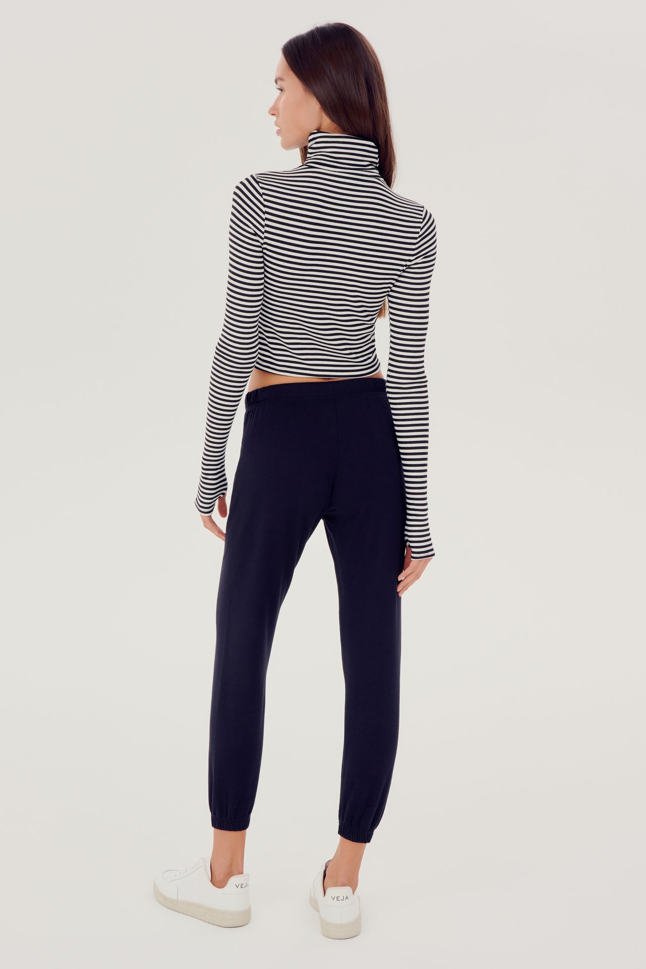 The back view of a woman wearing a black SPLITS59 Jackson Rib Cropped Turtleneck sweater and high waist leggings.