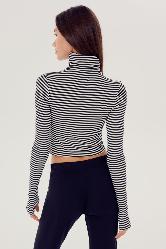 The back view of a woman wearing a black and white striped SPLITS59 Jackson Rib Cropped Turtleneck top.