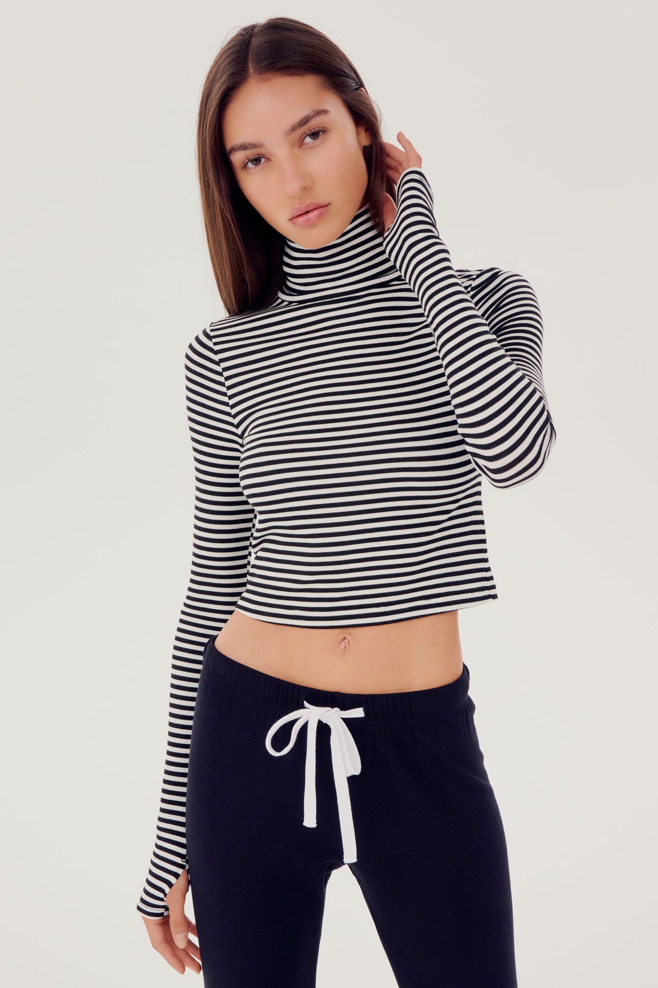The model is wearing a black and white striped SPLITS59 Jackson Rib Cropped Turtleneck top and black high waist leggings.