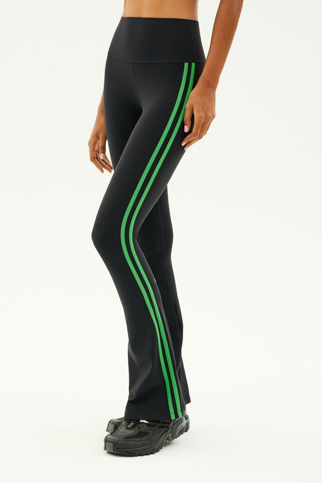 A person wearing the SPLITS59 Raquel High Waist Flared Legging in Black/Grass and black shoes, perfectly suited for workouts, stands against a plain background. The leggings' 4-way stretch design ensures maximum comfort and flexibility.