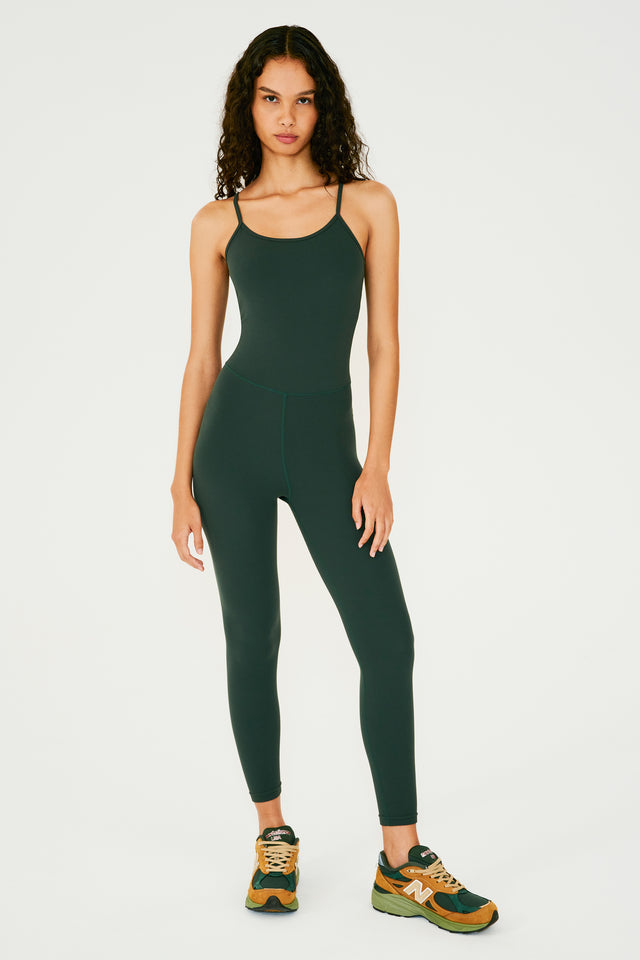 Full front view of girl wearing dark green one piece with leggings and spaghetti straps with multi colored shoes