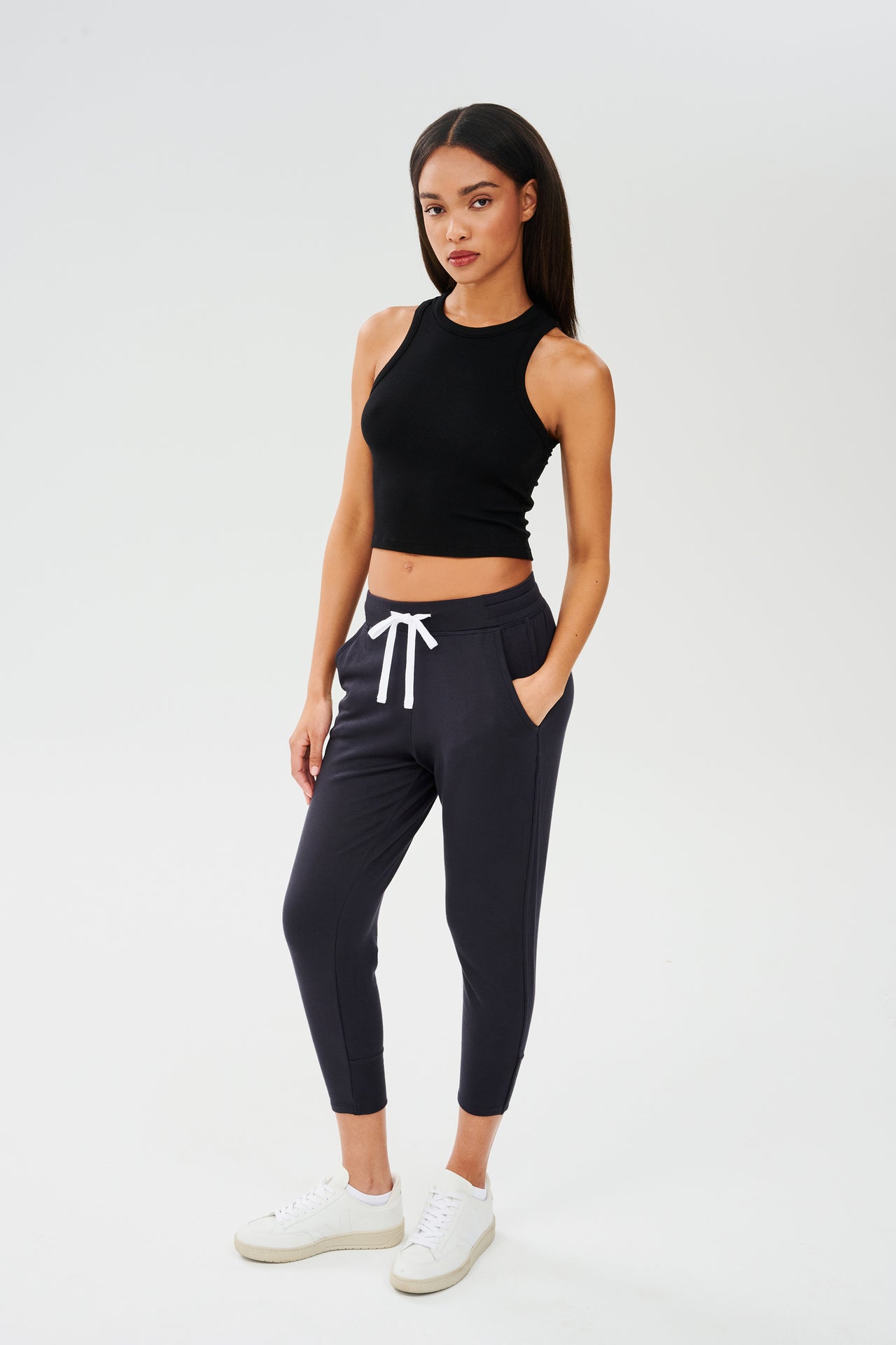 The model is wearing a SPLITS59 Kiki Rib Crop Tank - Black made of soft fabric and black joggers, perfect for gym workouts.