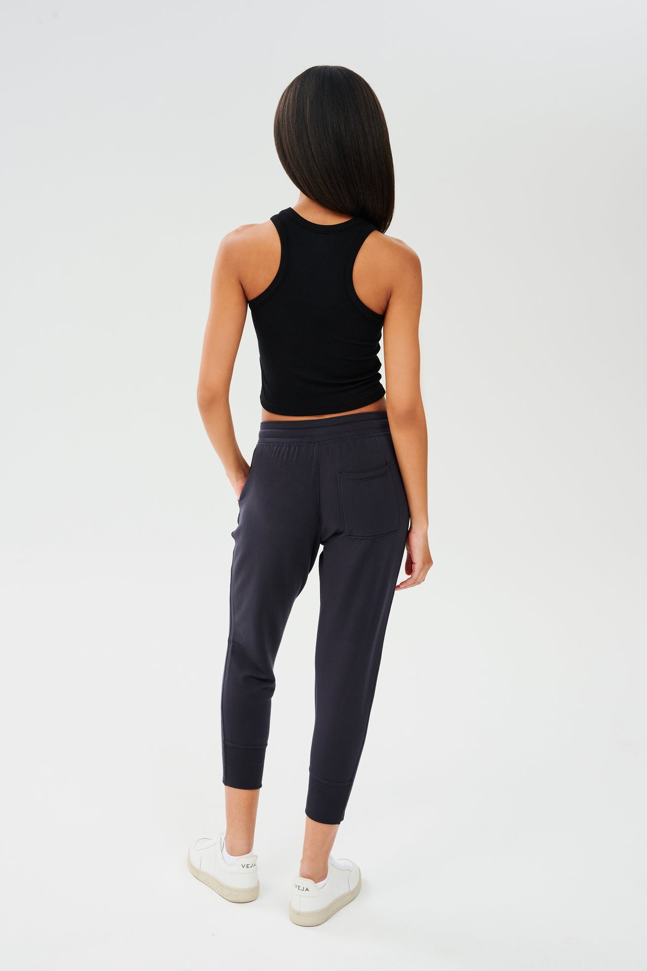 The back view of a woman wearing a SPLITS59 Kiki Rib Crop Tank - Black, designed for gym workouts, and black joggers.