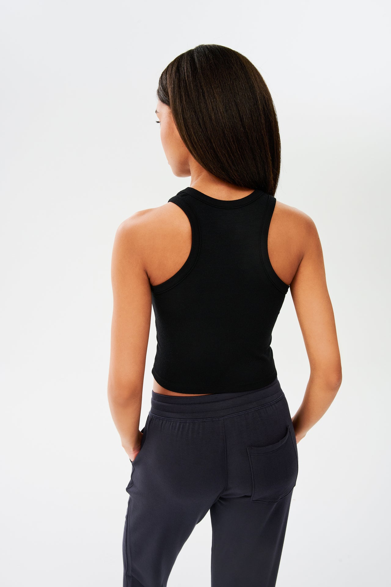The back view of a woman wearing a SPLITS59 Kiki Rib Crop Tank in Black and grey sweatpants, ideal for gym workouts.