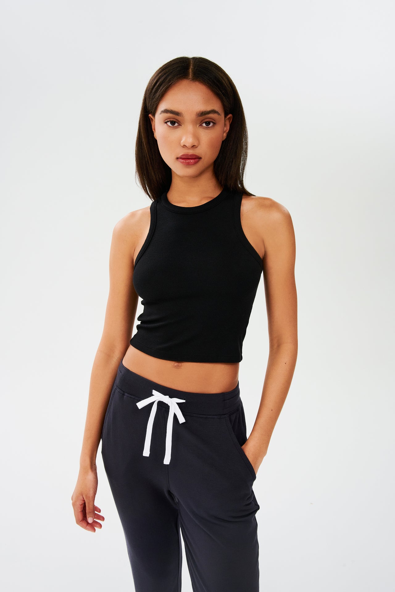 The model is wearing a black Kiki Rib Crop Tank from SPLITS59 and sweatpants made from soft fabric, perfect for gym workouts.