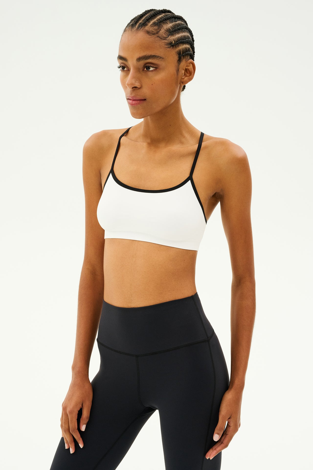 A person wearing the SPLITS59 Loren Seamless Bra in white and black, along with black leggings, stands against a plain background, making it ideal for gym workouts.