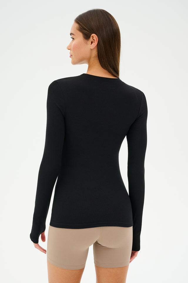 A woman in the SPLITS59 Louise Rib Long Sleeve top, colored black, and beige shorts stands facing away.