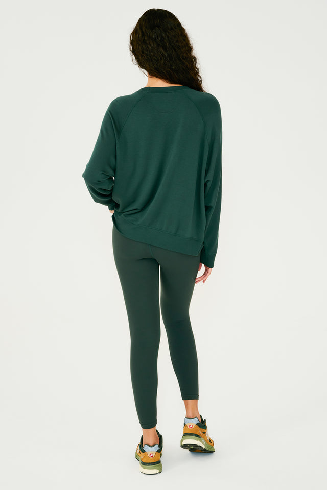 Full back view of girl wearing dark green sweatshirt with visible stitching and ribbed hem, with dark green leggings and multi colored shoes