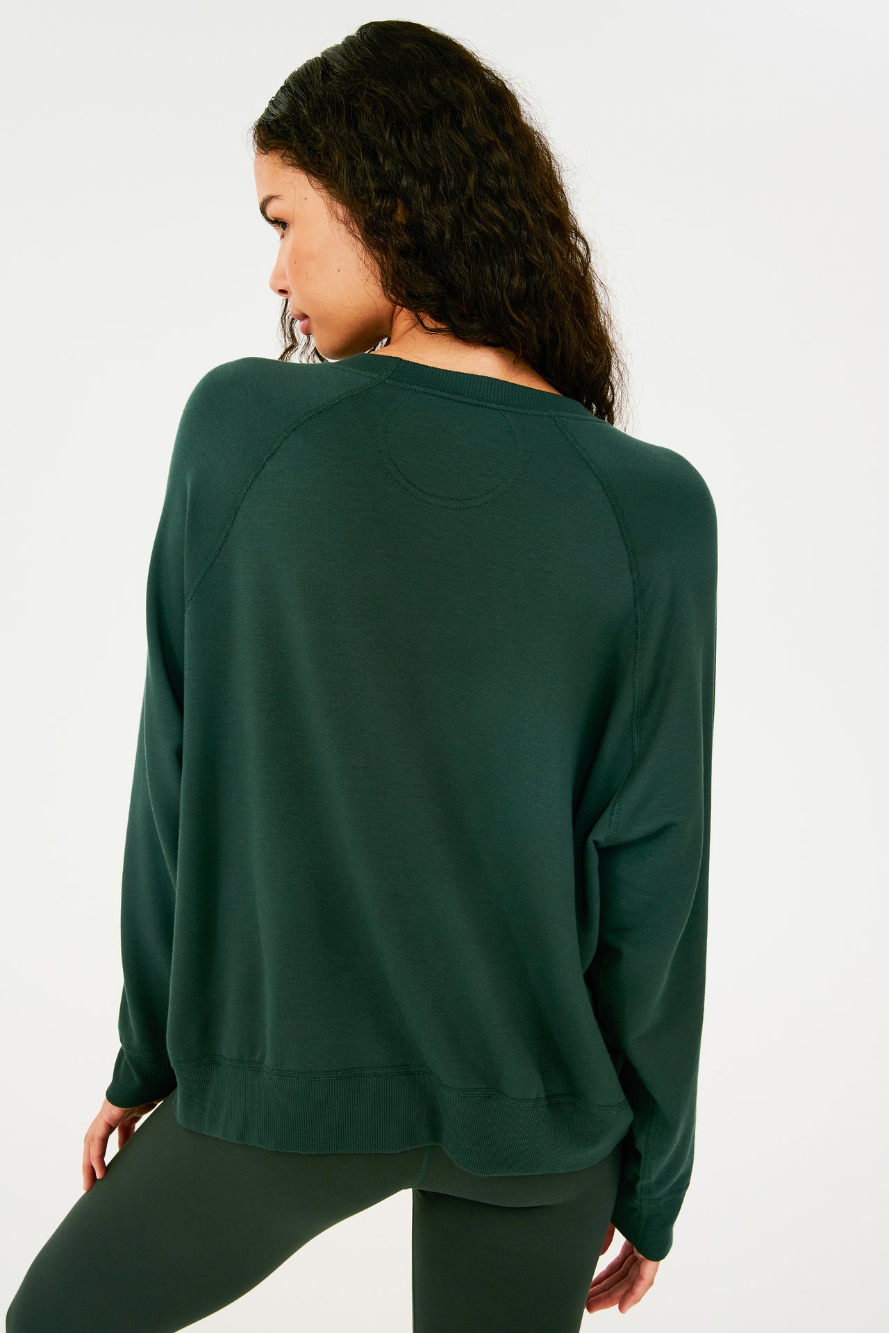 Back view of girl wearing dark green sweatshirt with visible stitching and ribbed hem