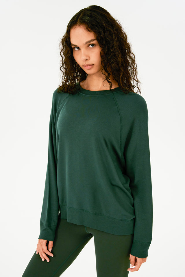 Side view of girl wearing dark green sweatshirt with visible stitching and ribbed hem