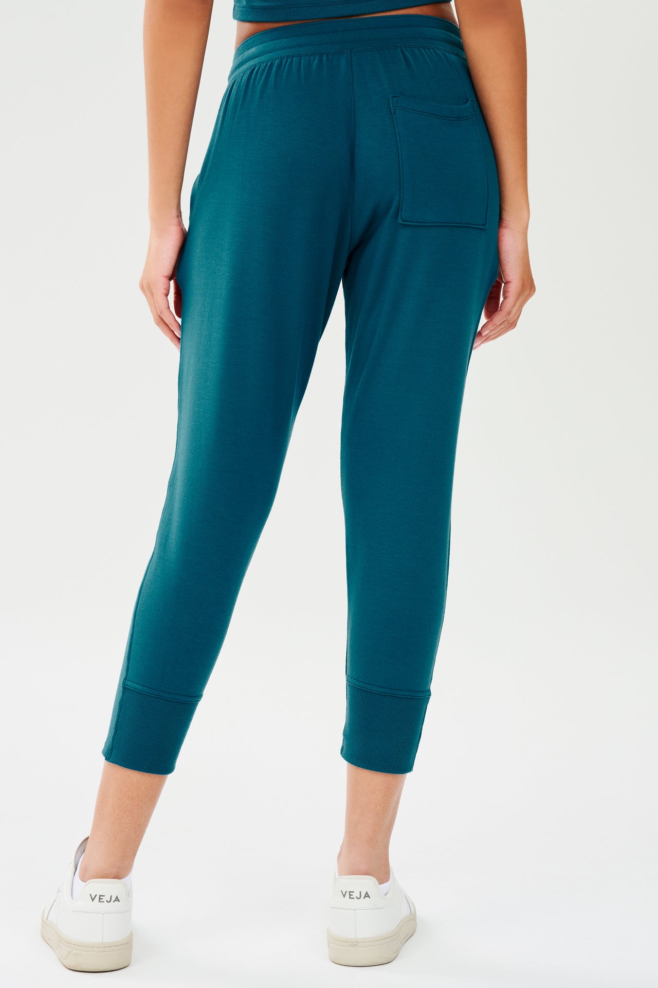 Back view of woman wearing a green and blue tone sweatpant with tapered leg and above ankle length with back pocket. Paired with white shoes.