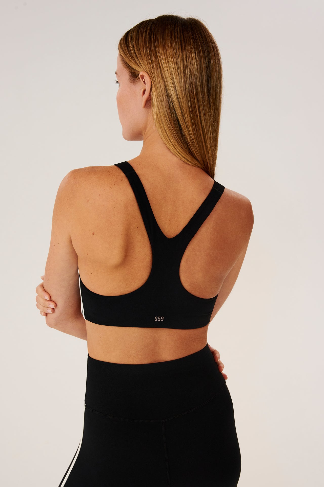 Back view of girl wearing black sports bra with two thin white stripes  down the side and black leggings