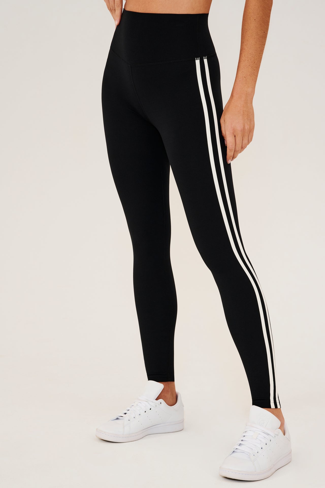 Side view of girl wearing black leggings with two thin white stripes down the side with white shoes