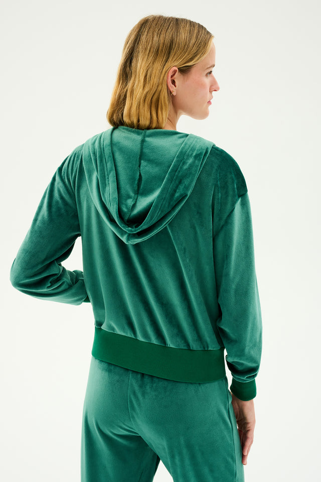 A person with shoulder-length blond hair is shown from the back, wearing a comfortable Rhys Velour Zip Up Hoodie in Arugula by SPLITS59 and matching pants.