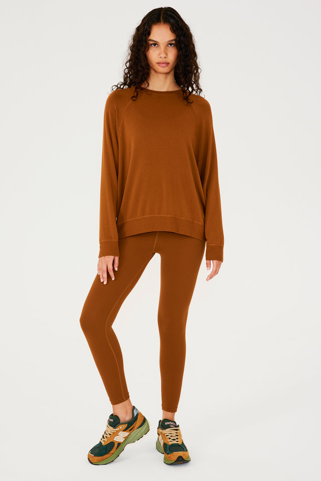 Full front view of girl wearing redish brown sweatshirt with visible stitching and ribbed hem, redish brown leggings and multi colored shoes