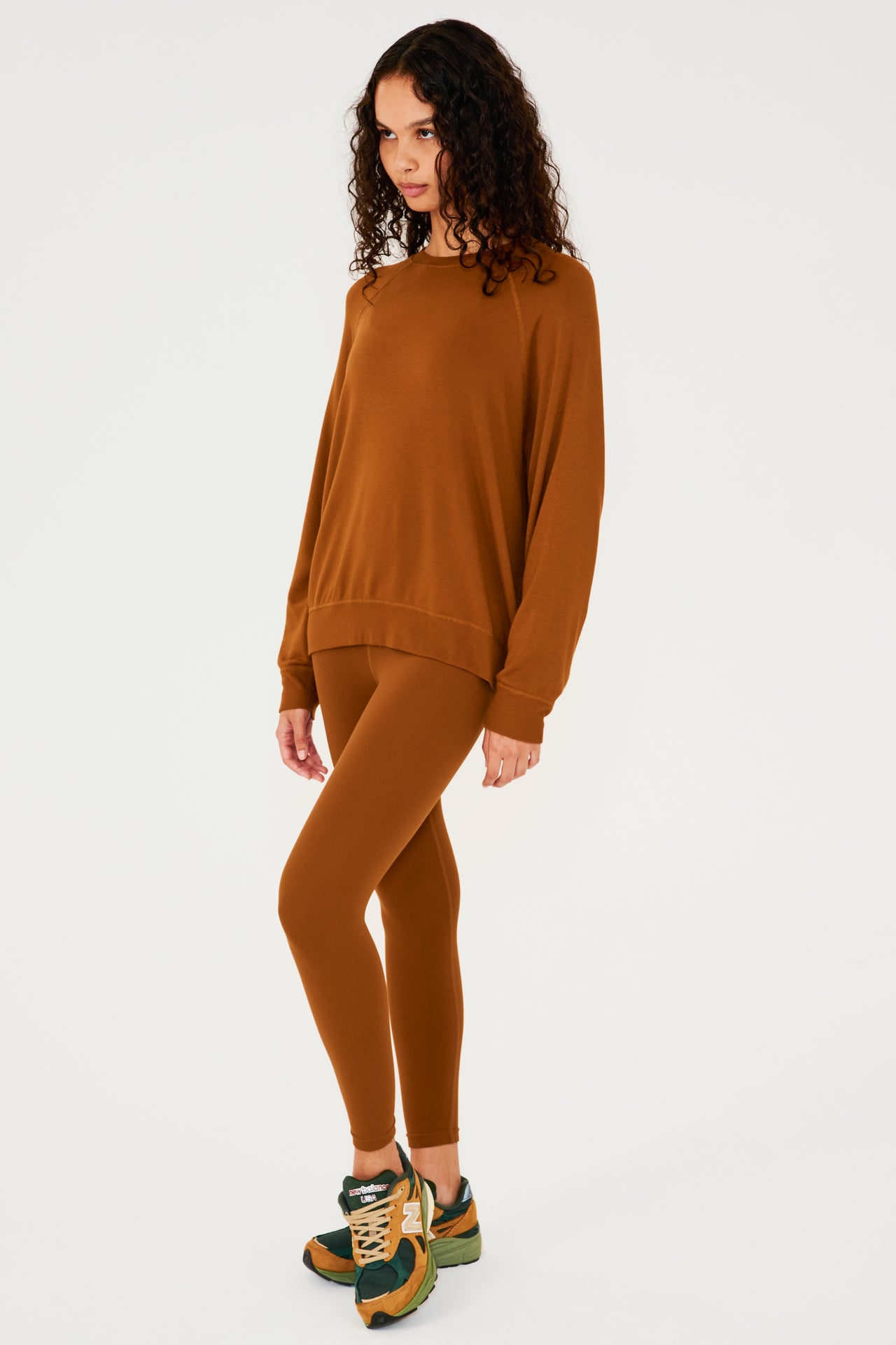 Full front view of girl wearing redish brown sweatshirt with visible stitching and ribbed hem and multi colored shoes