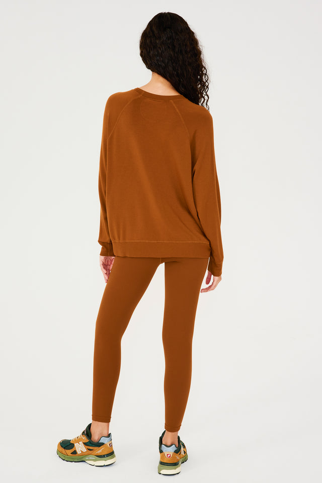 Full back view of girl wearing redish brown sweatshirt with visible stitching and ribbed hem, redish brown leggings and multi colored shoes
