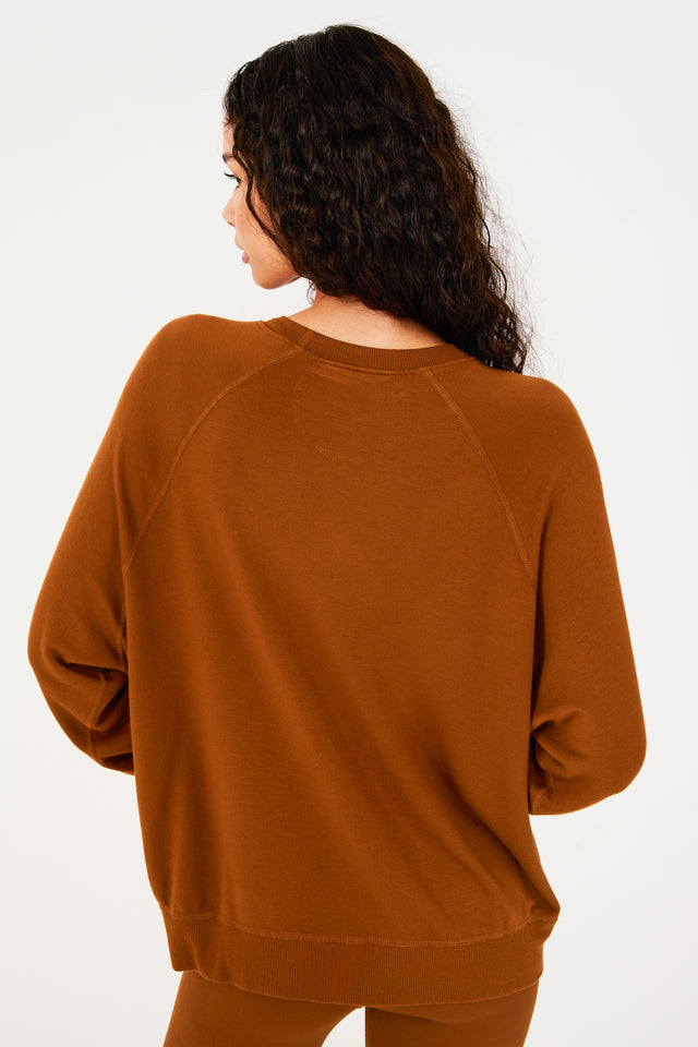 Back view of girl wearing redish brown sweatshirt with visible stitching and ribbed hem