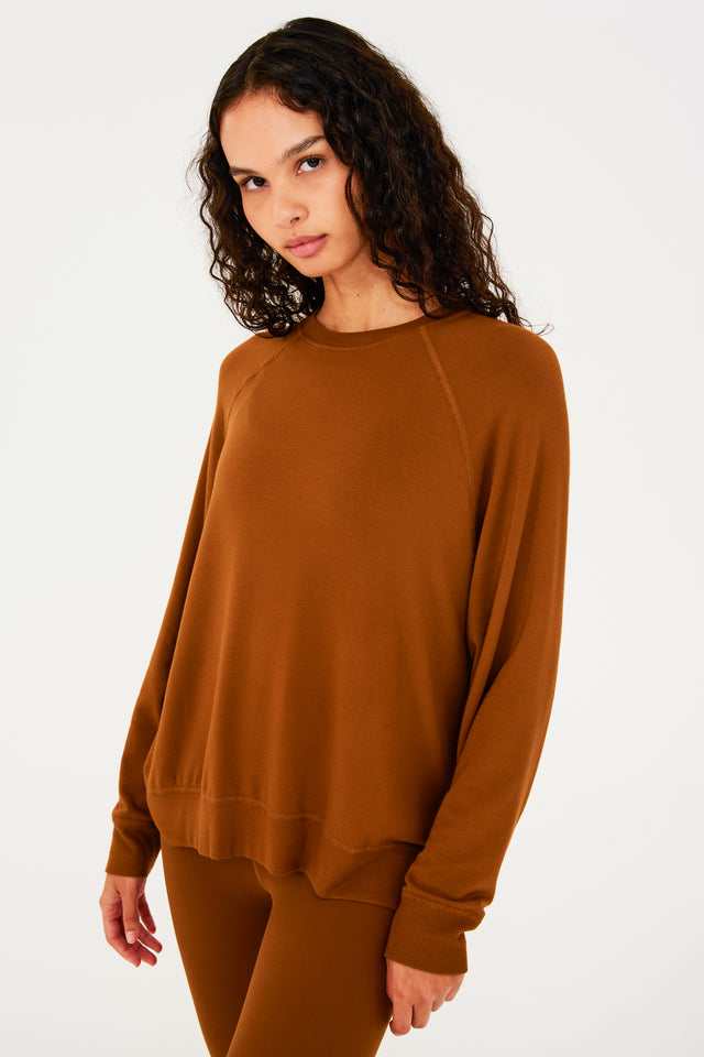 Side view of girl wearing redish brown sweatshirt with visible stitching and ribbed hem