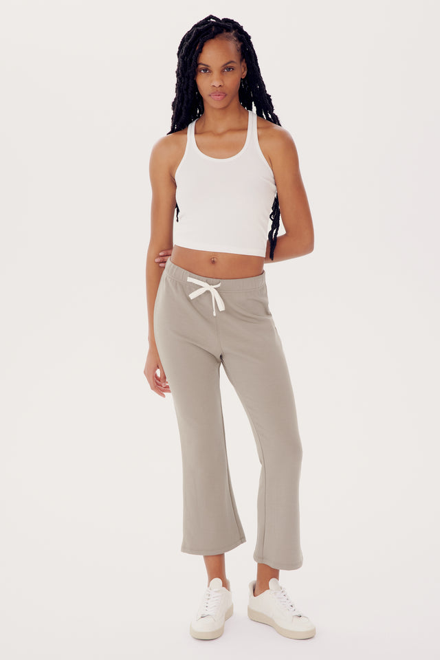 A woman in a white tank top and beige SPLITS59 Fleece Cropped Flare - Latte pants stands against a white background.