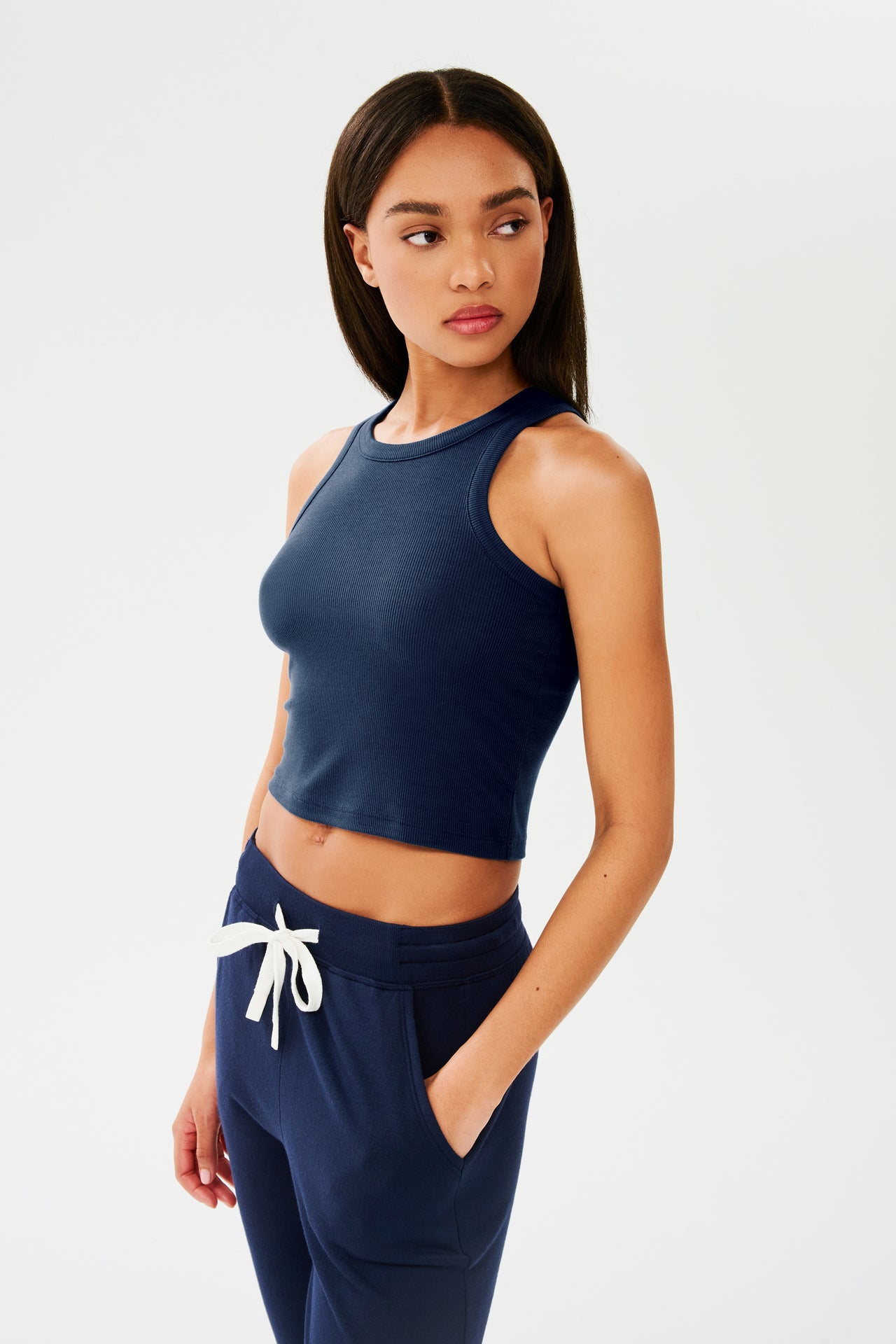 The model is wearing a Kiki Rib Crop Tank in Indigo and white sweatpants ideal for gym workouts by SPLITS59.
