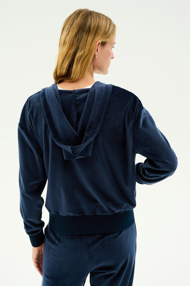 A person with long blonde hair is shown from the back, wearing the SPLITS59 Rhys Velour Zip Up Hoodie in indigo along with matching pants, epitomizing both comfort and versatility.