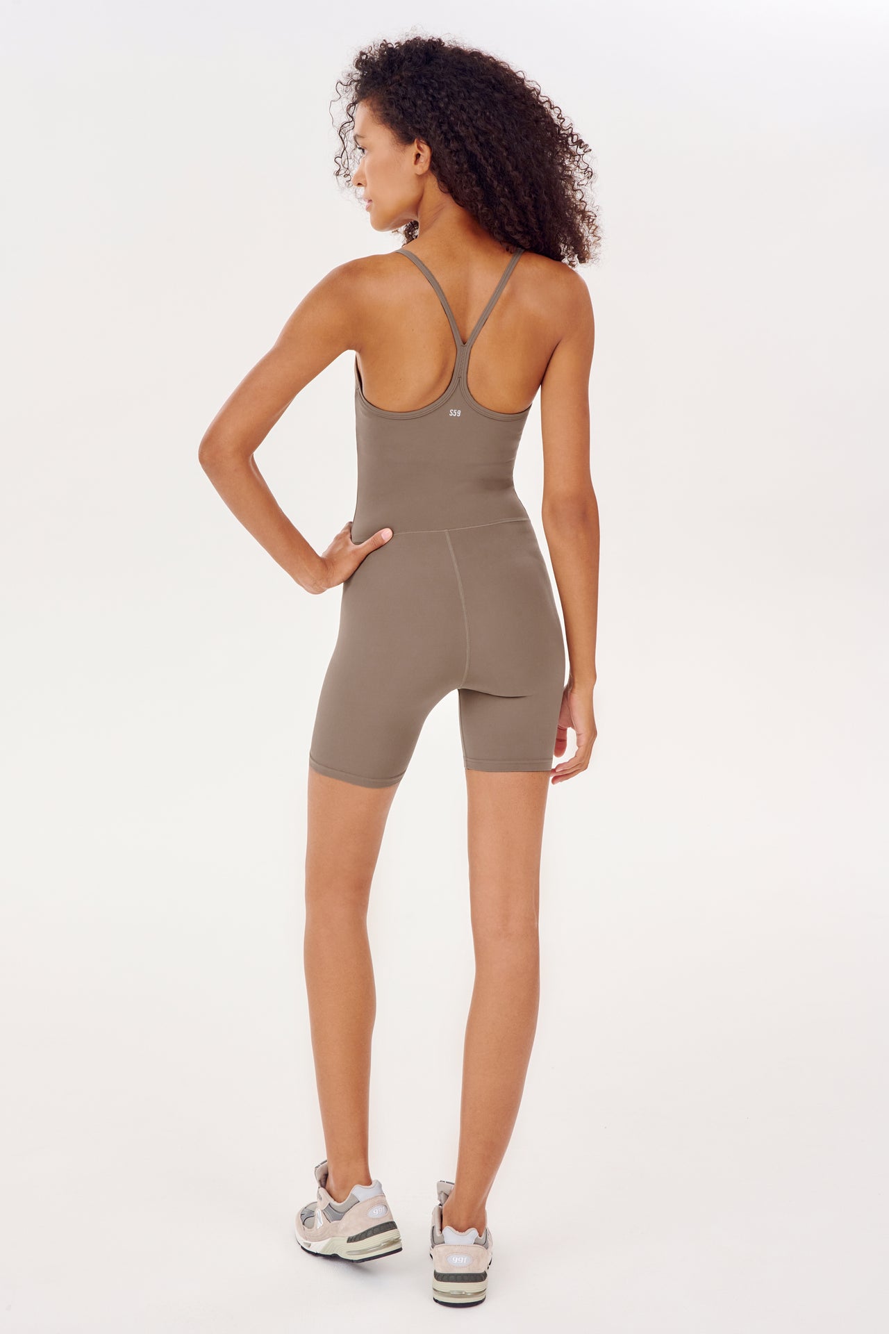 The back view of a woman in a SPLITS59 Airweight 6” Short Jumpsuit - Lentil.
