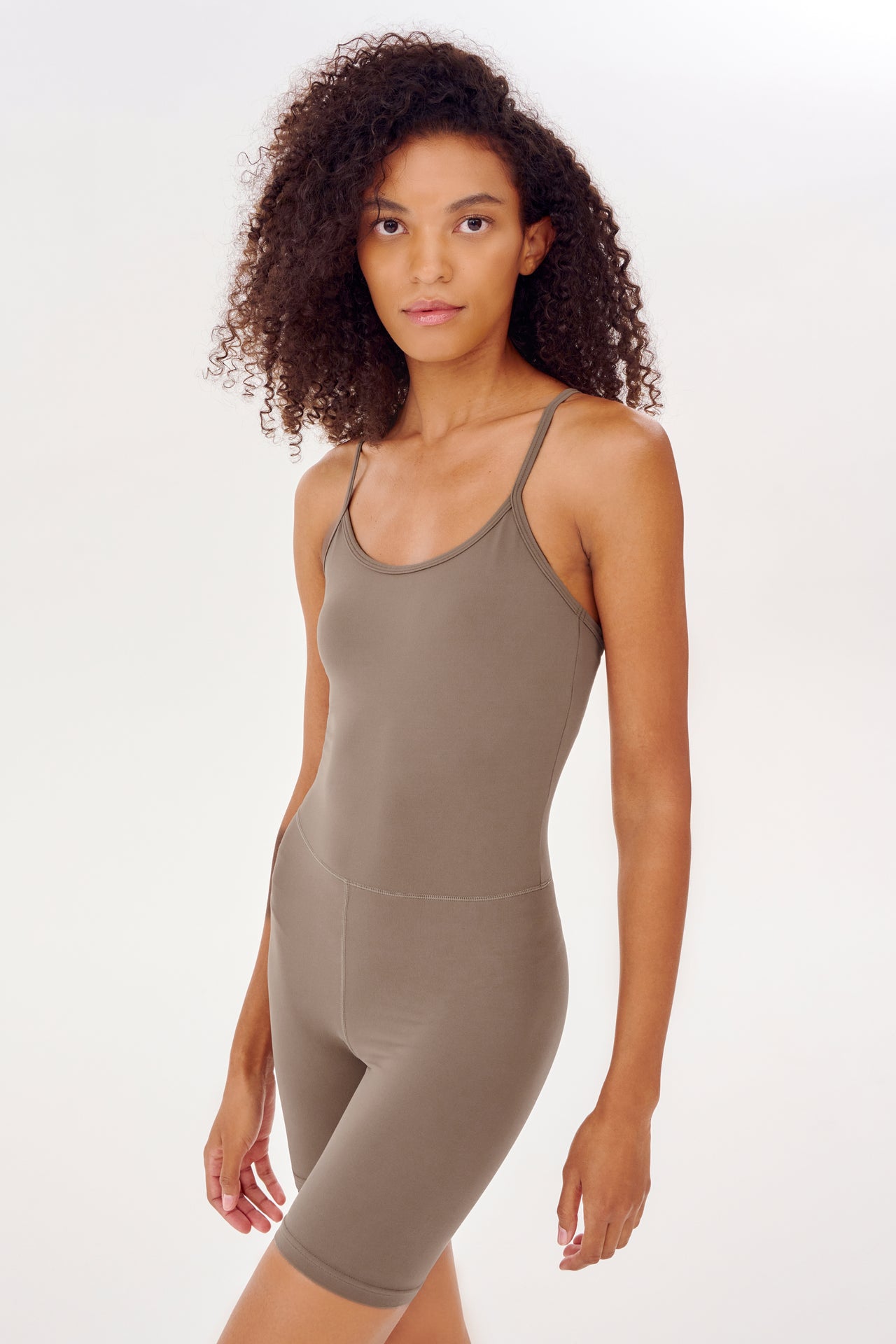 A woman in a tight brown Airweight 6” Short Jumpsuit made by SPLITS59.