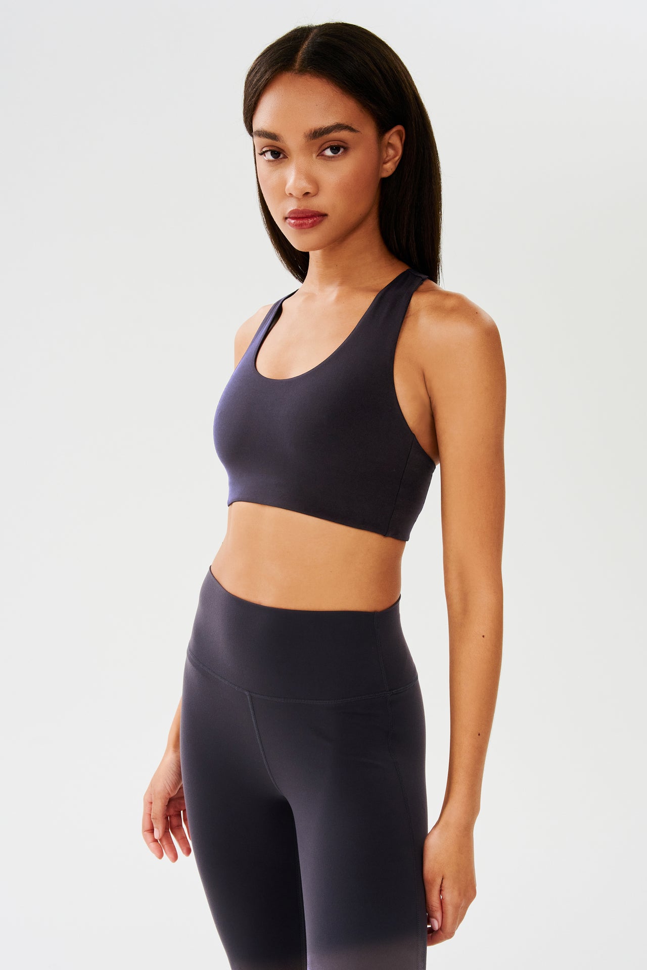 Front side view of woman with straight dark hair wearing dark gray with dark blue tone bra and dark gray with dark blue tone leggings