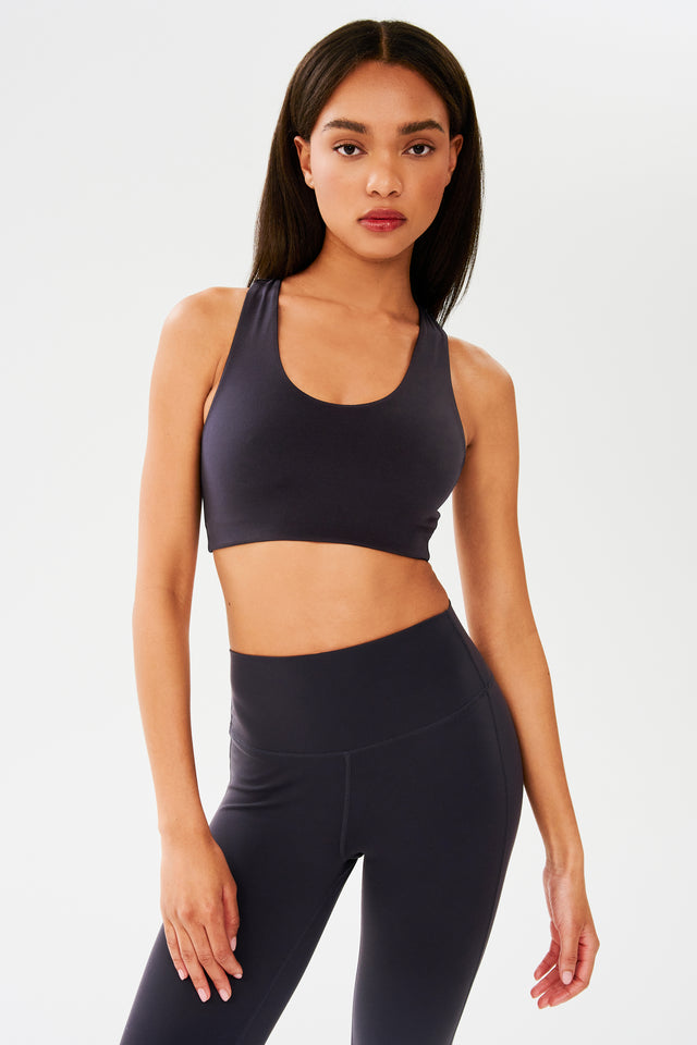 Full front view of woman with straight dark hair wearing dark gray with dark blue tone bra and dark gray with dark blue tone leggings