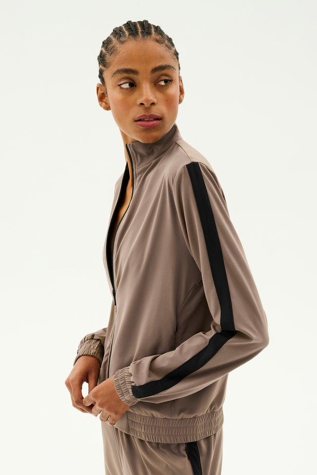 A person is wearing the Max Rigor Track Jacket in Lentil and Black, part of the SPLITS59 collection, standing and looking to the side against a plain background.