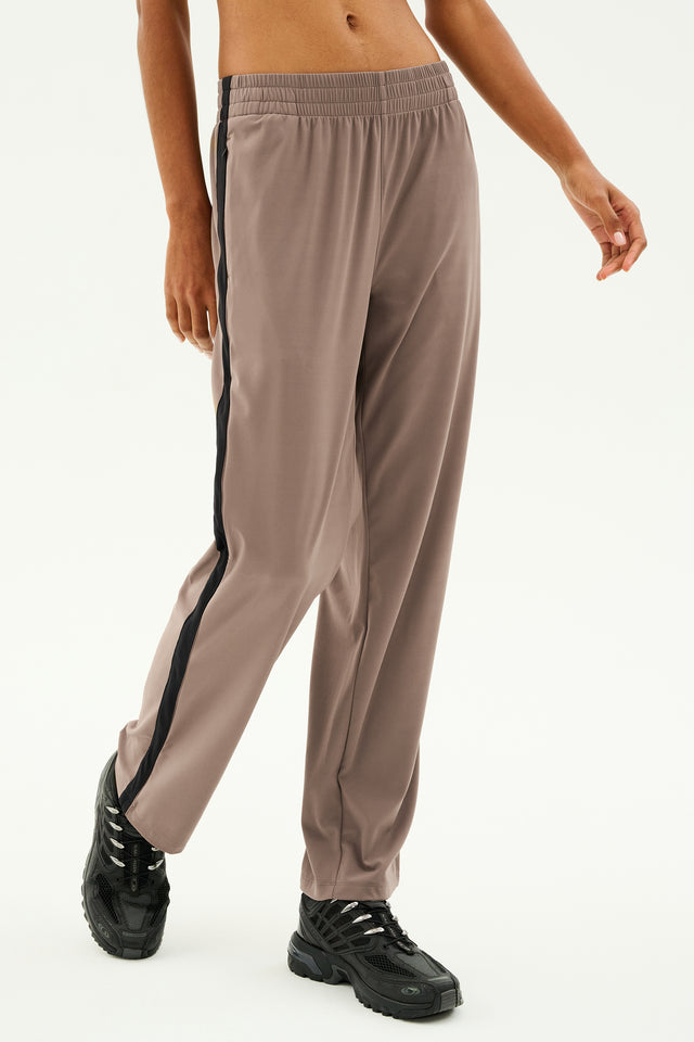 A person wearing the Max Rigor Track Pant by SPLITS59 in Lentil/Black paired with black sneakers, standing against a plain background. The wide leg design of the track pants adds a touch of flair, effortlessly combining comfort and style.