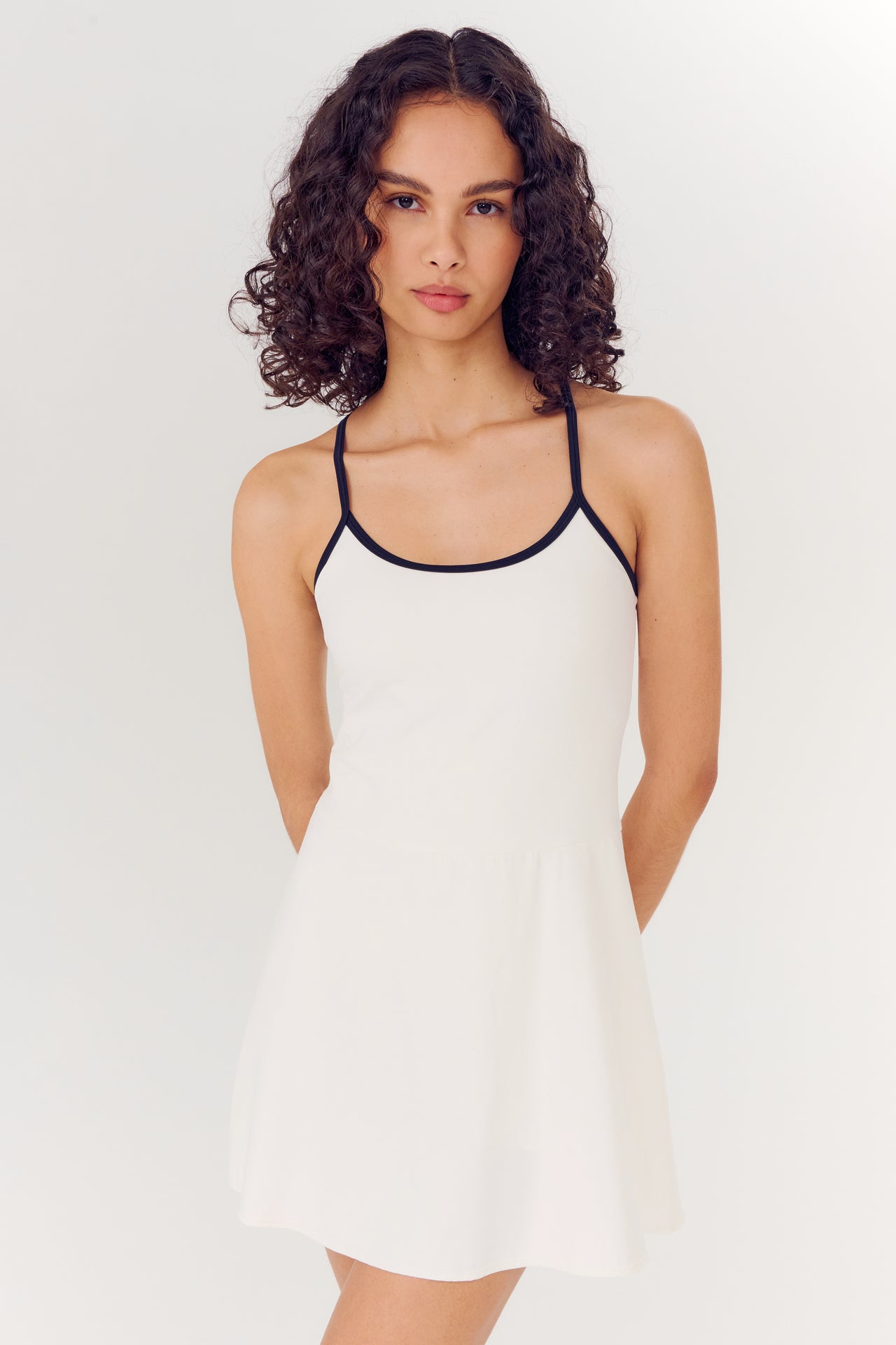 A woman in a Simona Airweight Tank Dress in White/Indigo by SPLITS59 with black trim stands against a plain background.