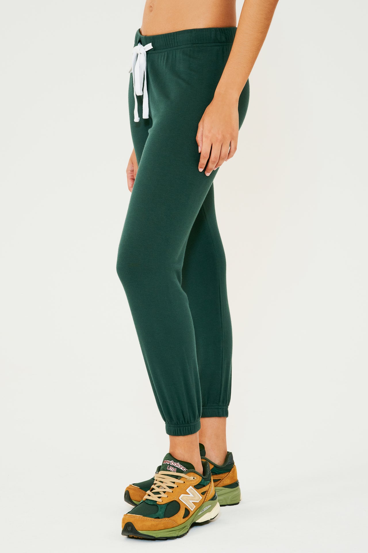 Front side view of woman wearing dark green sweatpant jogger paired with dark green, orange and light green shoes
