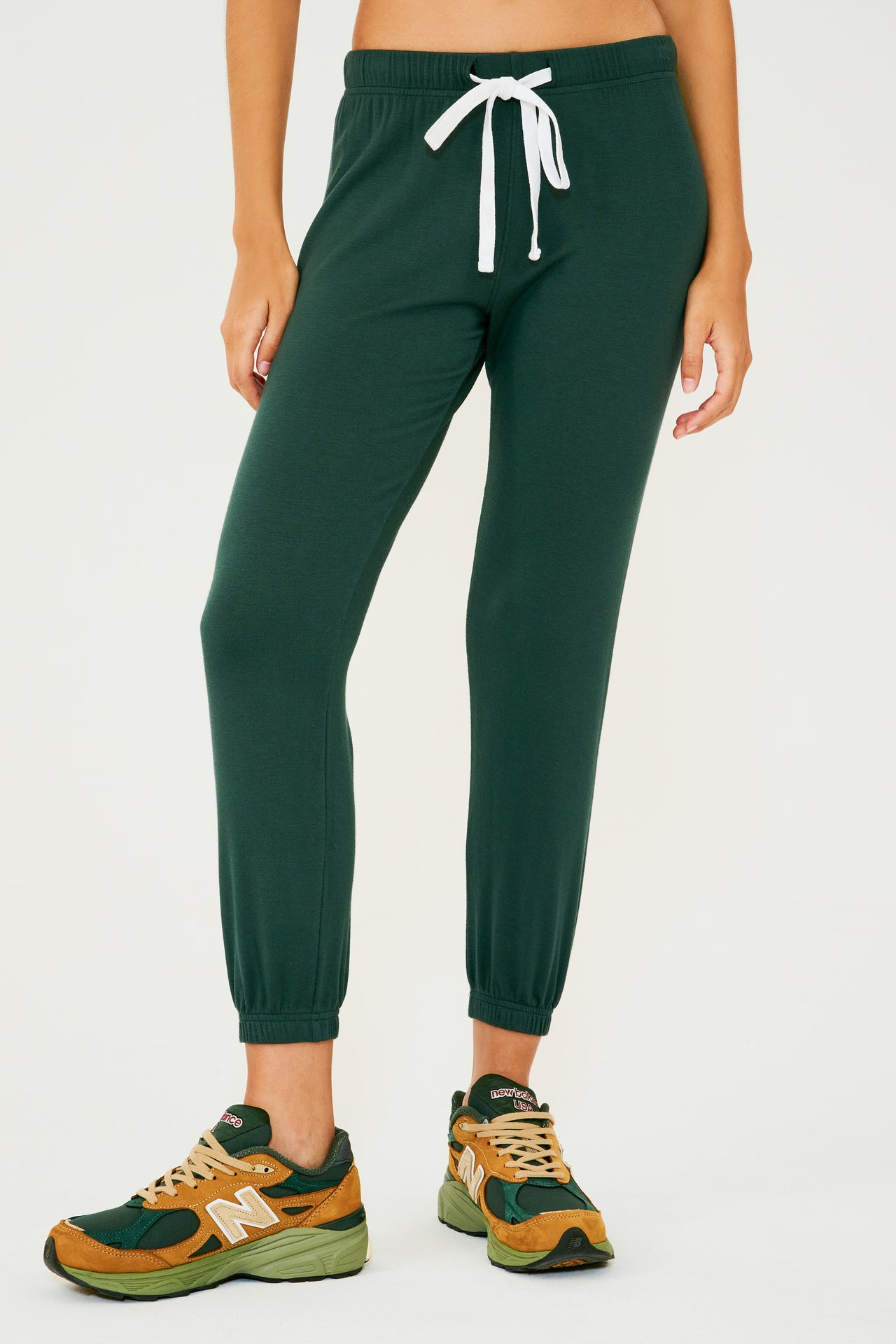 Front view of woman wearing dark green sweatpant jogger paired with dark green, orange and light green shoes
