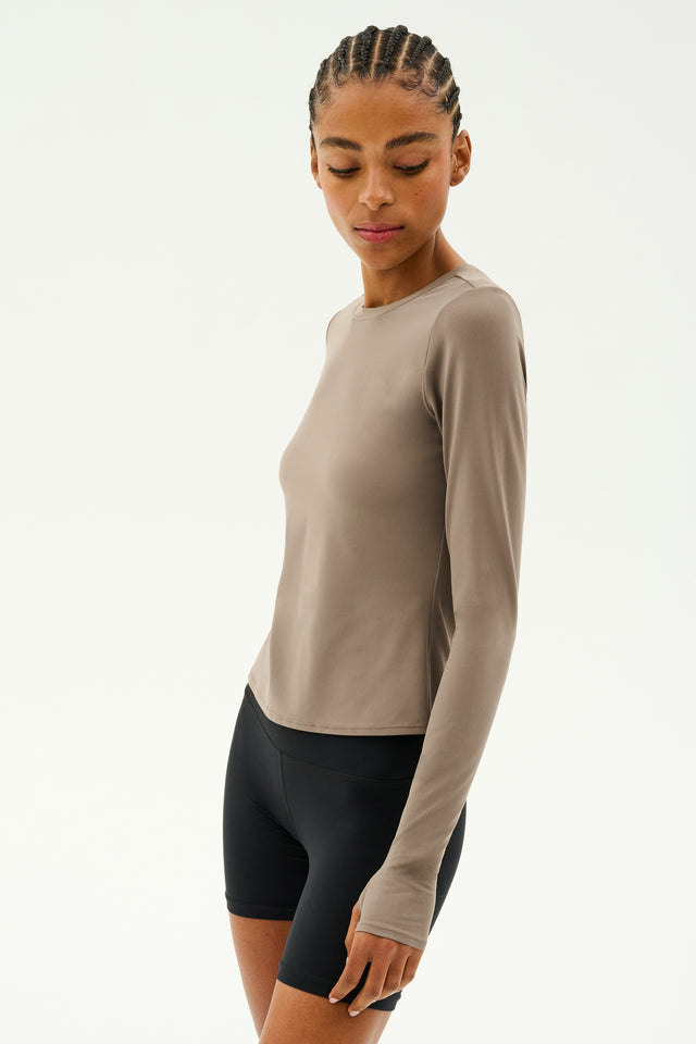 A person wearing a Lentil Airweight Lite long-sleeve waist-length top by SPLITS59 and quick-dry black shorts stands against a plain light background, ready for workouts.