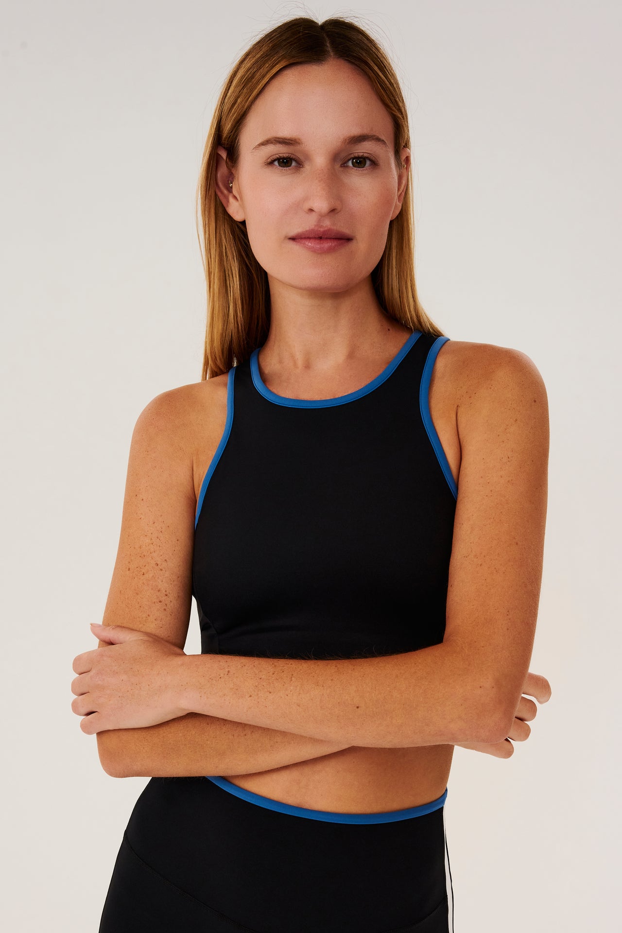 Front view of girl wearing black sports bra with blue hem and black leggings with blue stripe around the waistband and white stripe down the outer seam 