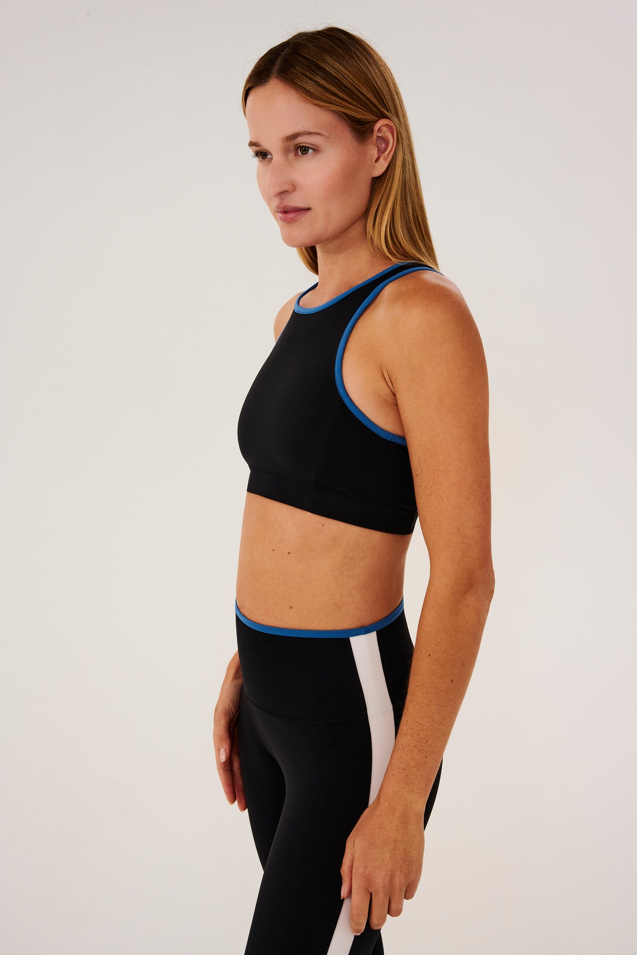 Side view of girl wearing black sports bra with blue hem and black leggings with blue stripe around the waistband and white stripe down the outer seam