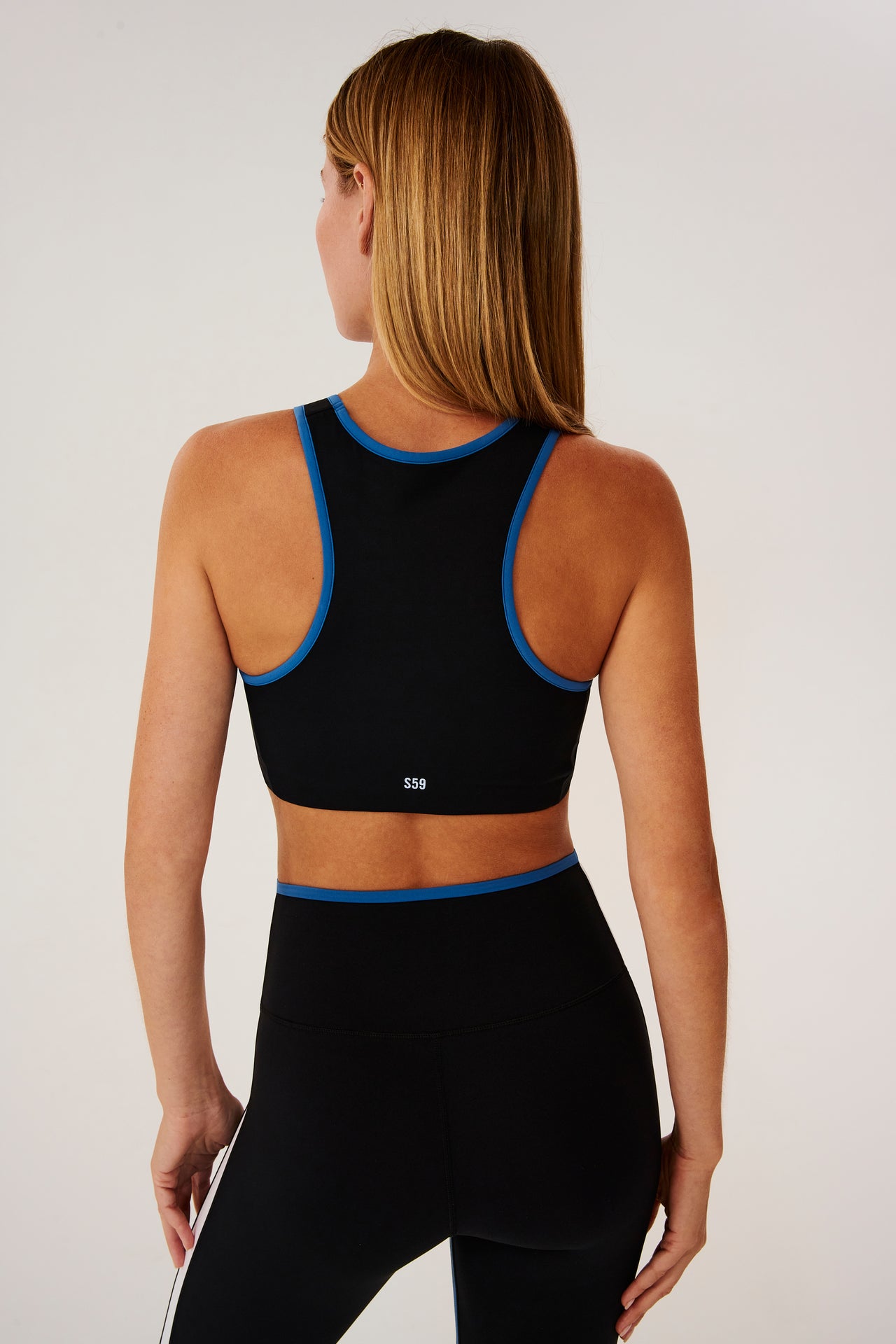 Back view of girl wearing black sports bra with blue hem and black leggings with blue stripe around the waistband and white stripe down the outer seam