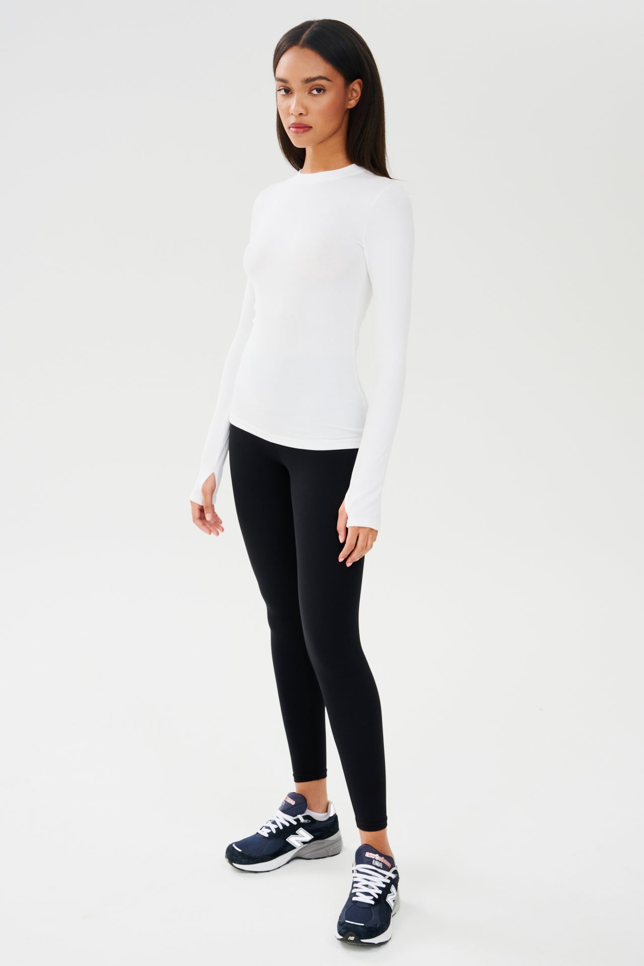 A woman wearing a SPLITS59 Louise Rib Long Sleeve in White and black leggings, perfect for yoga or gym workouts.
