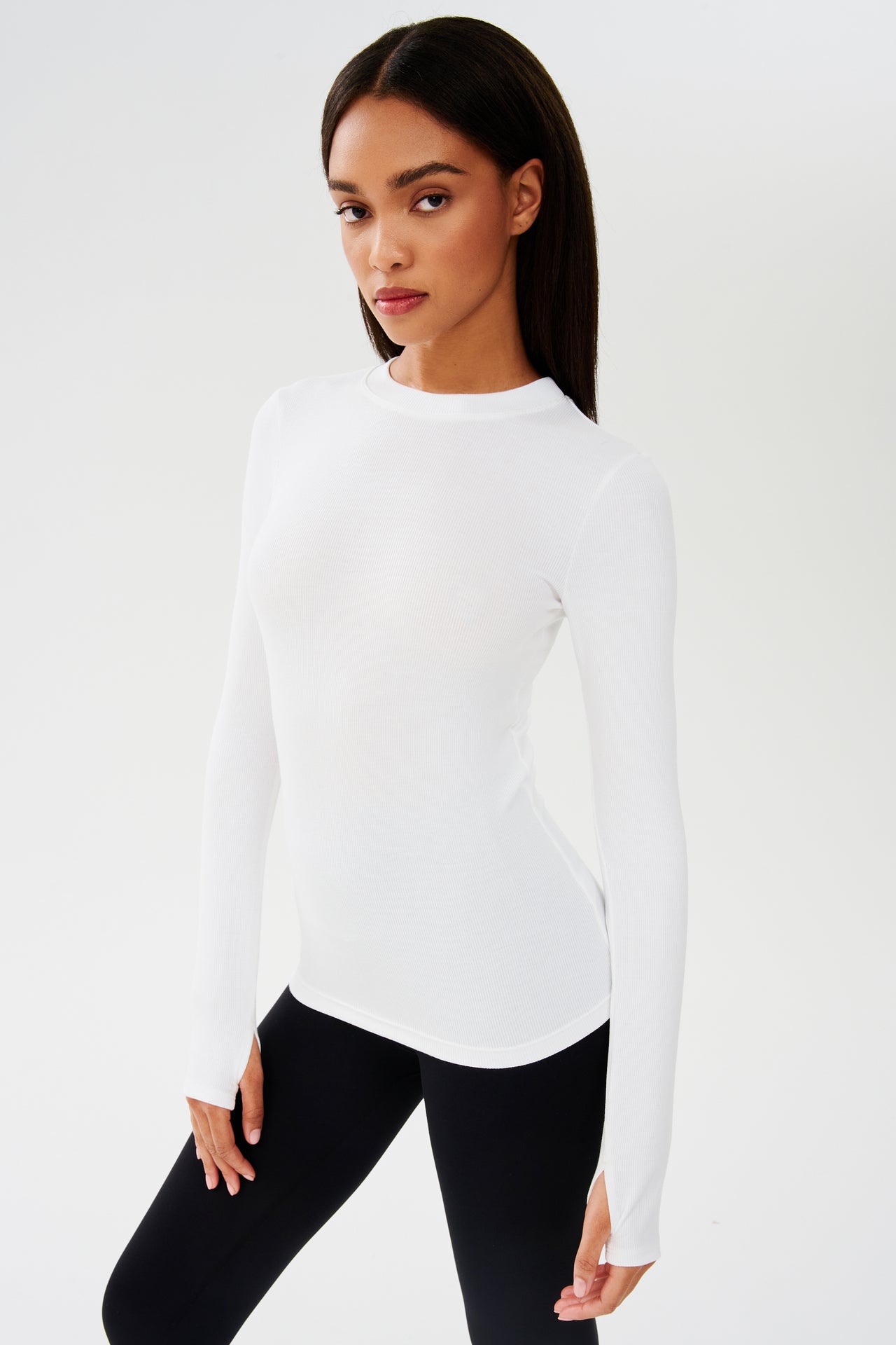 A model wearing a SPLITS59 Louise Rib Long Sleeve - White designed for yoga and black leggings.