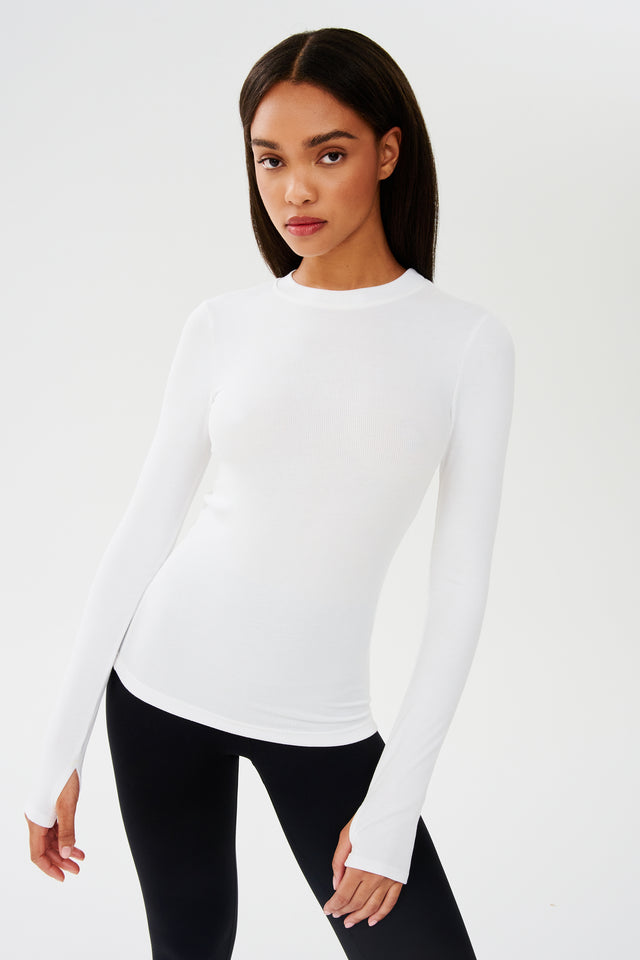 The model is wearing a SPLITS59 Louise Rib Long Sleeve - White designed for yoga and gym workouts, along with black leggings.